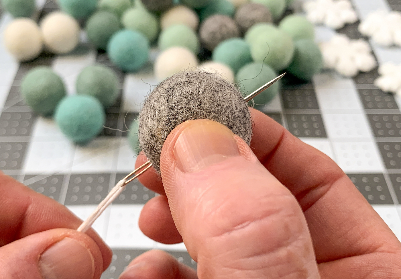 Pushing a needle through a gray felt ball