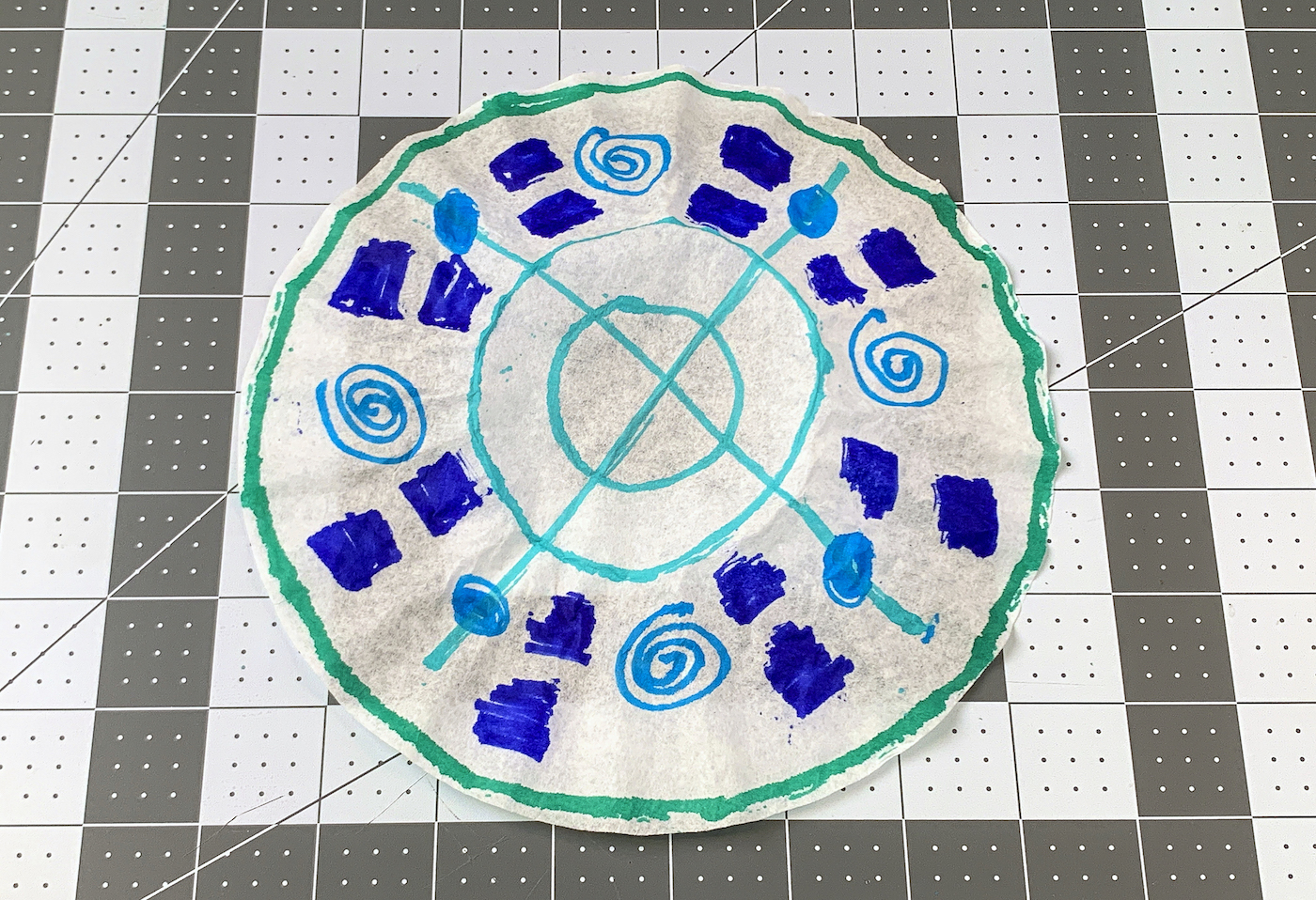 Coffee filter with marker lines drawn on it in green, blue, and aqua markers