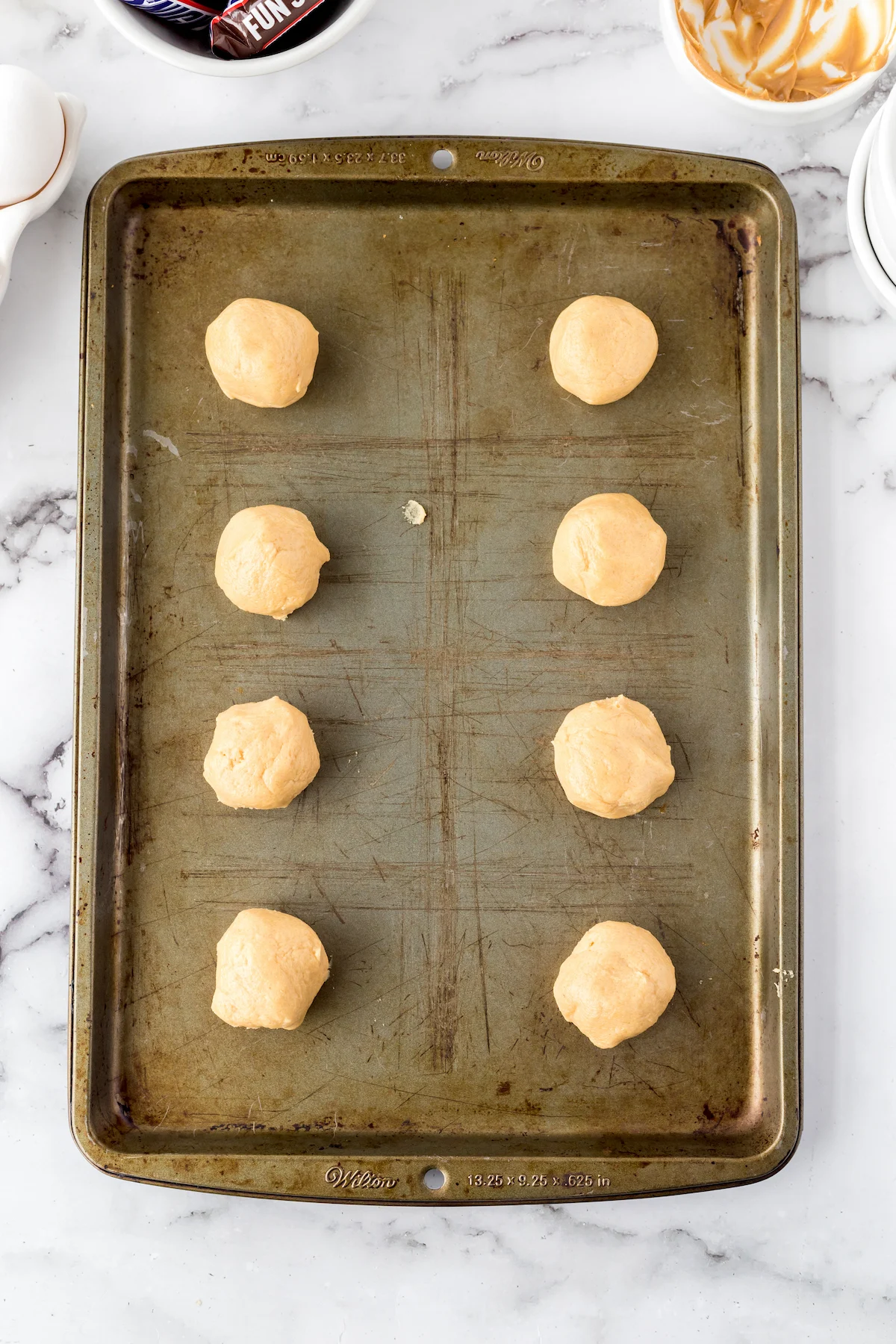 Balls of raw Snicker cookie dough on a cookie sheet