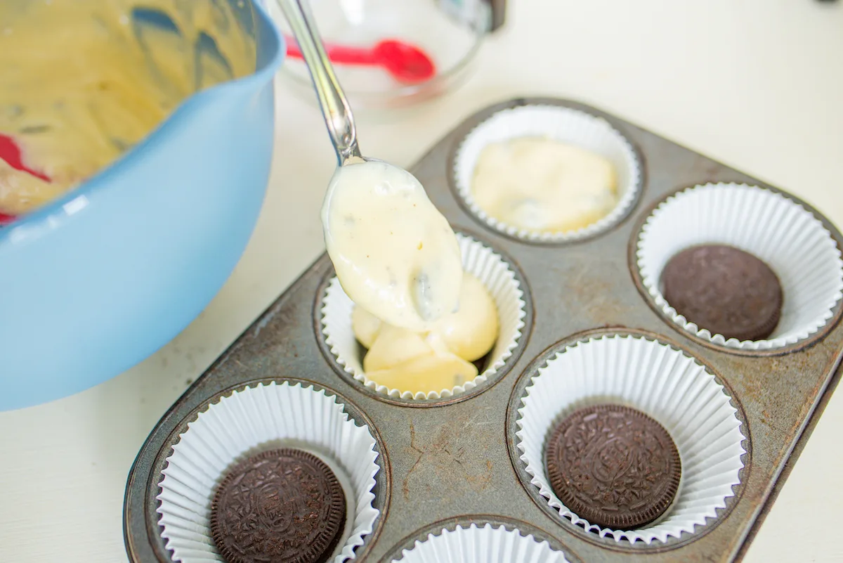 Adding batter to the cupcake tin with the Oreos
