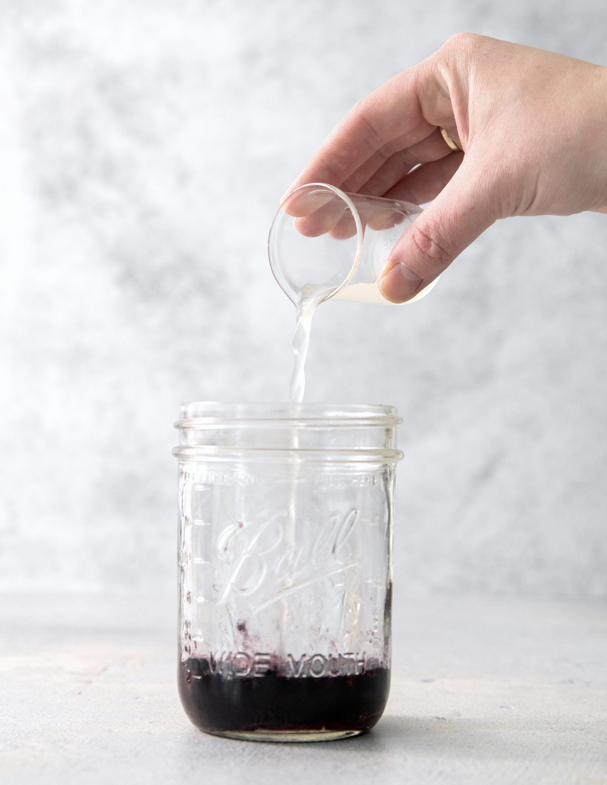 Adding liquor to the mason jar with simple syrup and blackberries