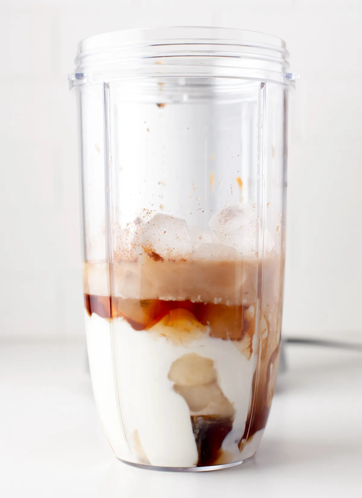 Blender filled with yogurt, almond milk, banana, pumpkin puree, maple syrup, ice