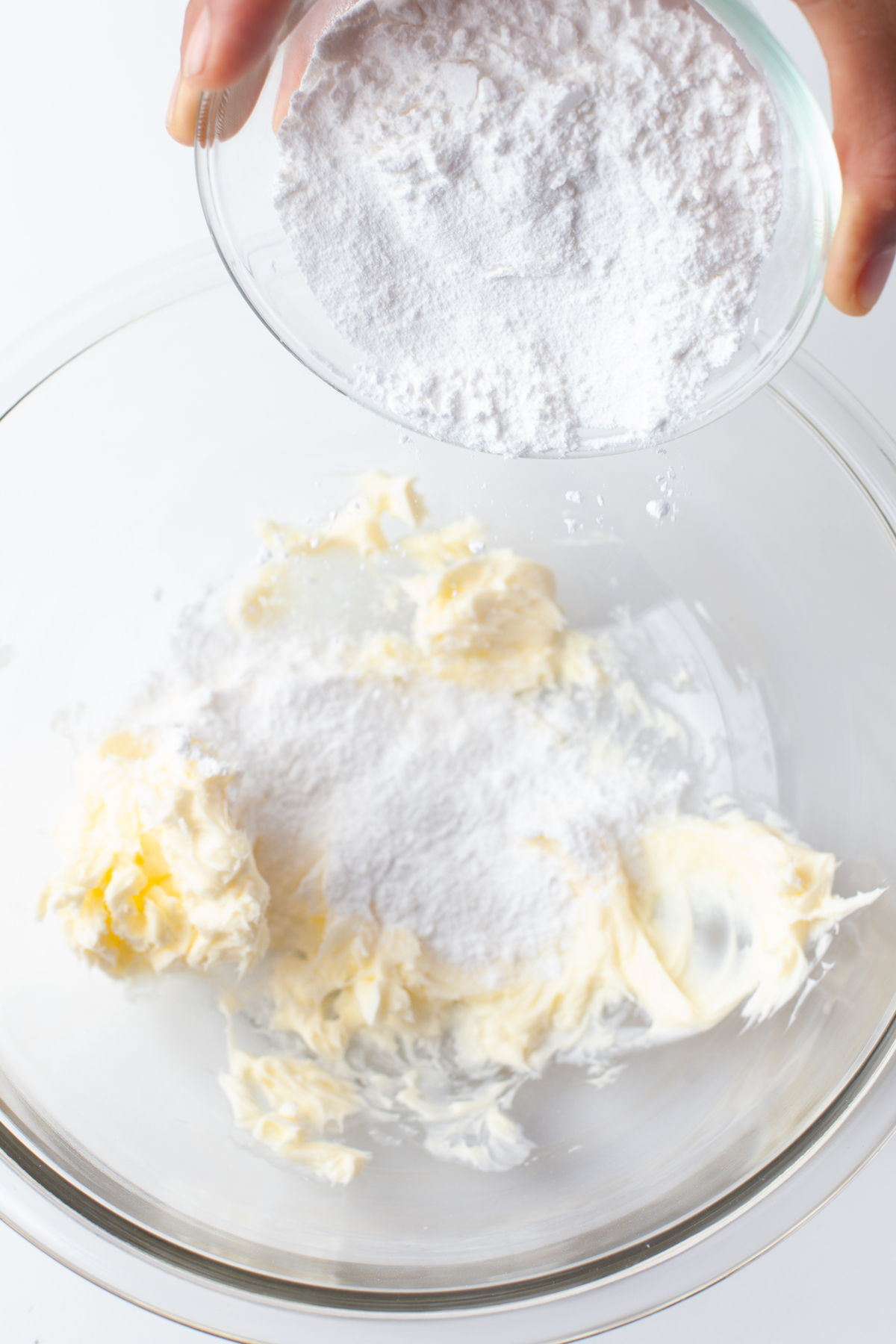 Dry ingredients being added to the creamed butter and sugar in a glass bowl