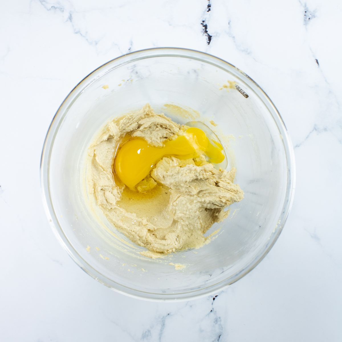Egg and vanilla added to the cookie batter in a clear glass bowl