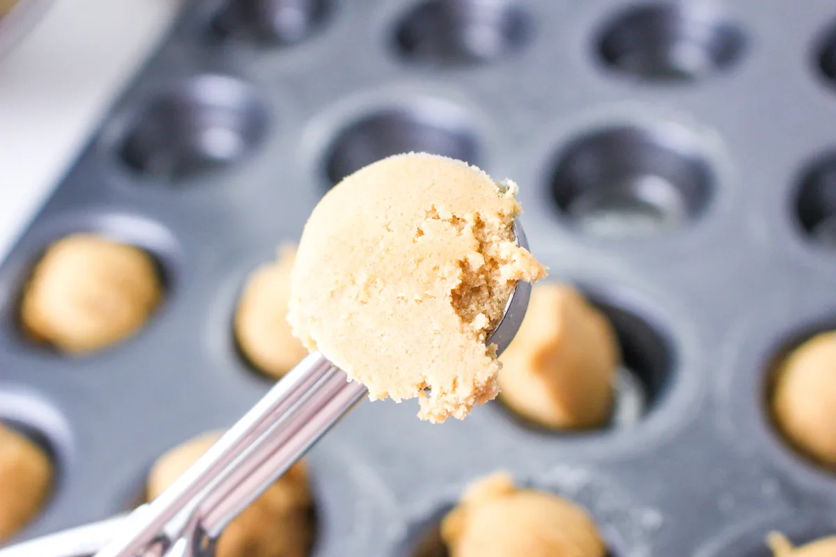 Scooping peanut butter dough into a mini muffin pan