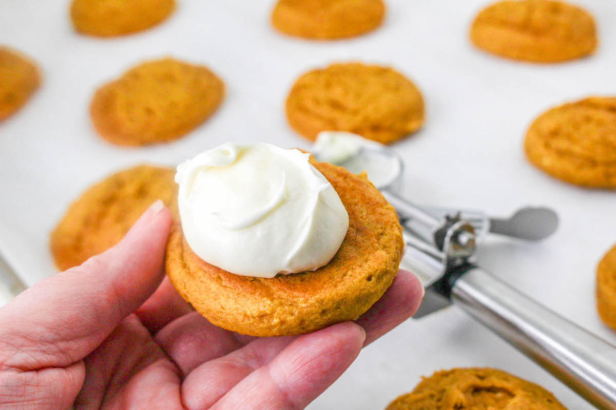 Spreading cream cheese icing onto the pumpkin cookies