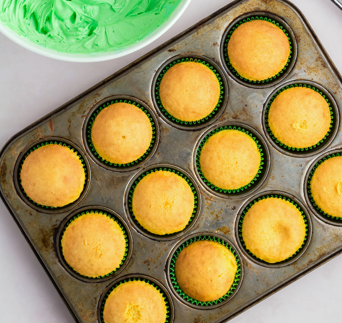 Baked vanilla cupcakes with a bowl of green icing