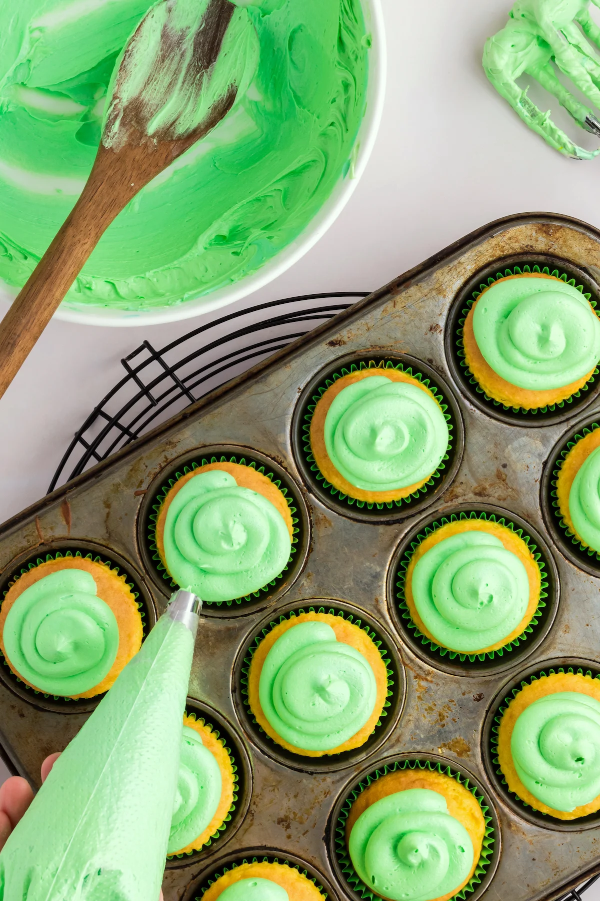 Frosting vanilla cupcakes with green frosting using a piping bag