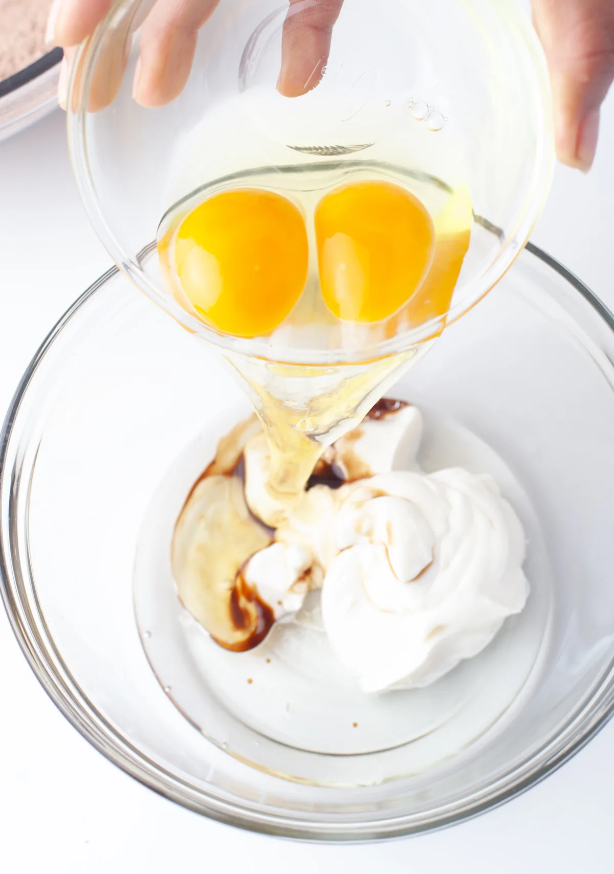Mixing eggs, vanilla, yogurt, and oil in a clear glass bowl