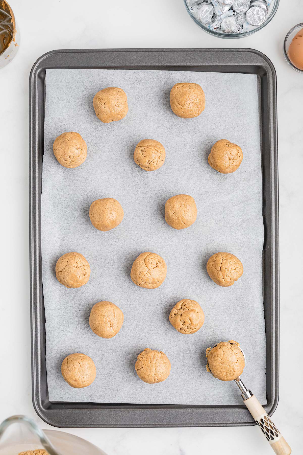 Peanut butter dough balls being placed on a cookie sheet