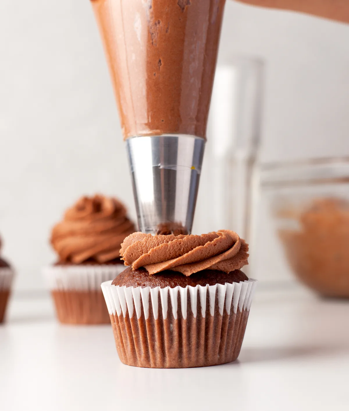 Piping chocolate frosting onto chocolate cupcakes