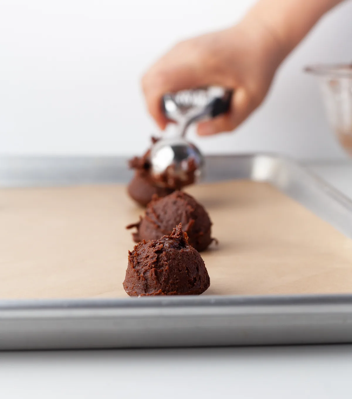 Scooping chocolate cookie dough onto a cookie sheet with a cookie scoop
