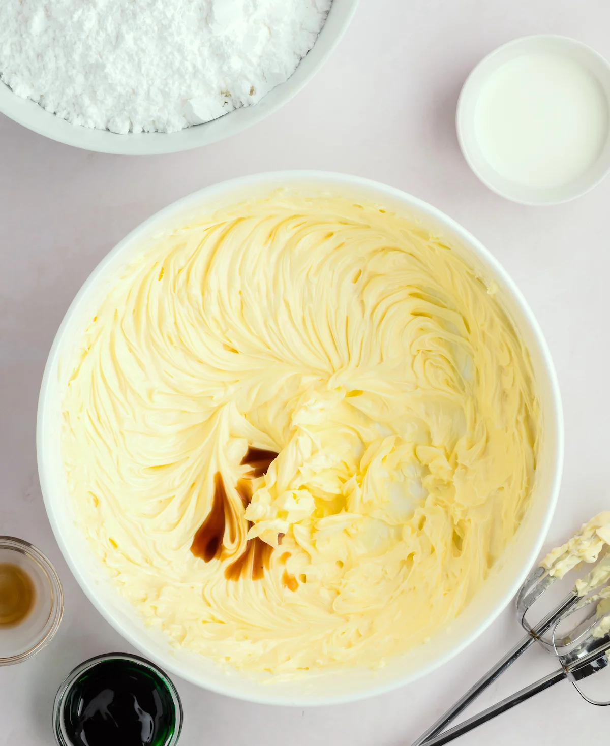 Vanilla extract added to creamed butter in a white ceramic bowl