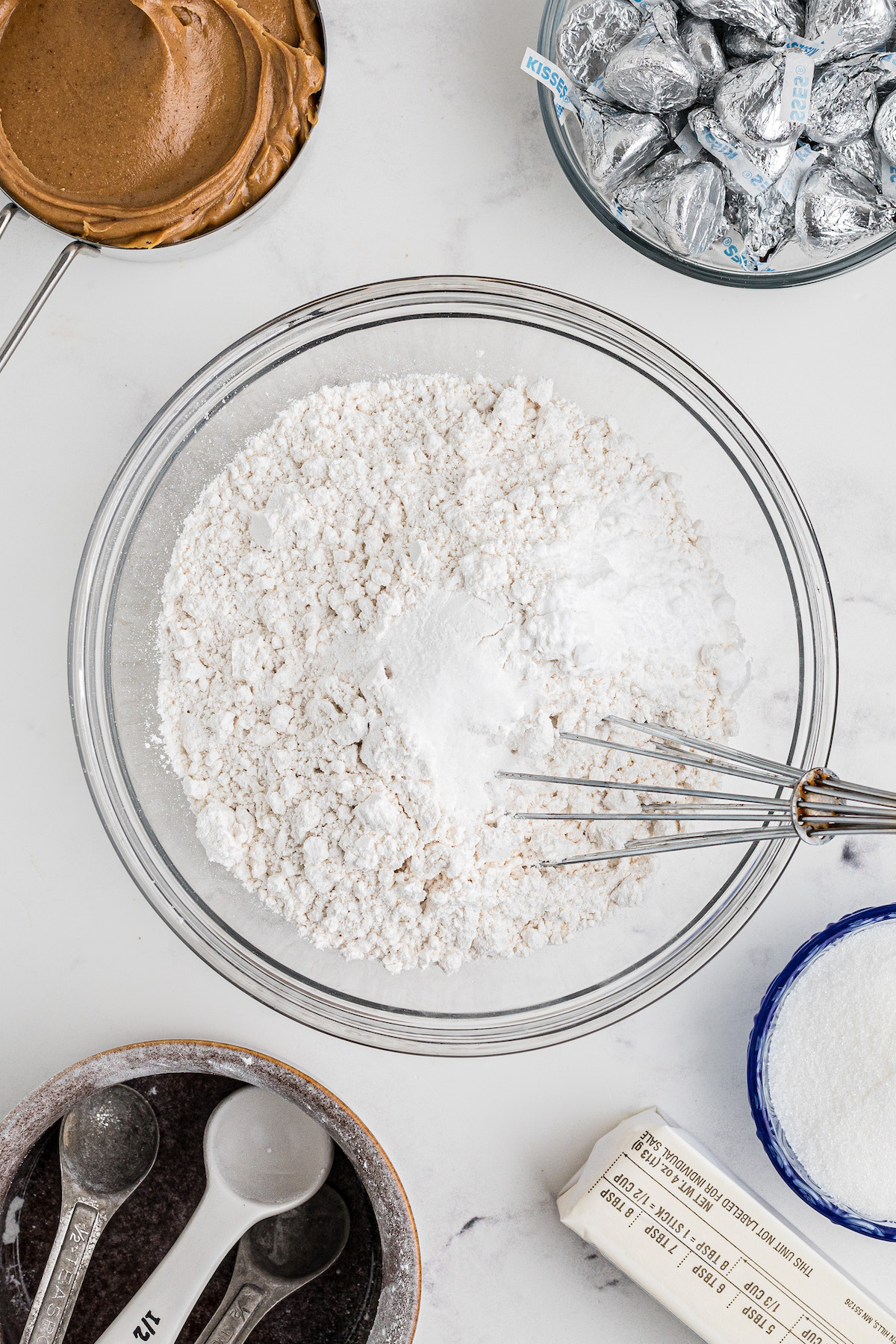 flour, baking powder, baking soda and salt being mixed in a bowl