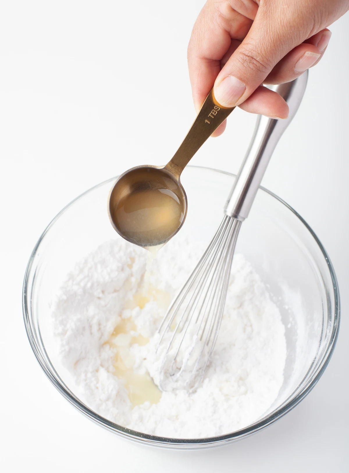 Adding lemon juice to powdered sugar in a clear glass bowl