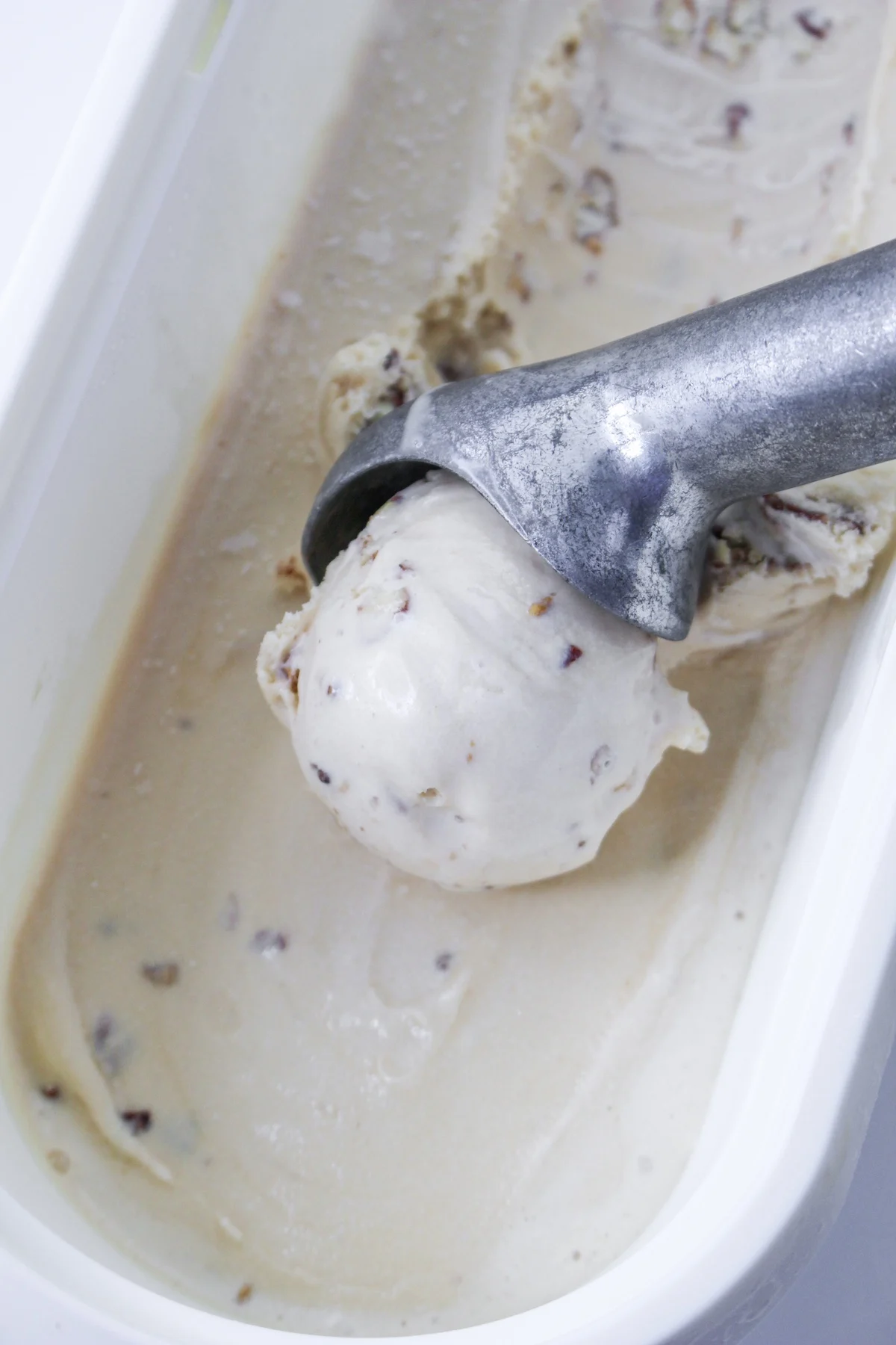 Butter and pecan ice cream being scooped out of a container with an ice cream scoop