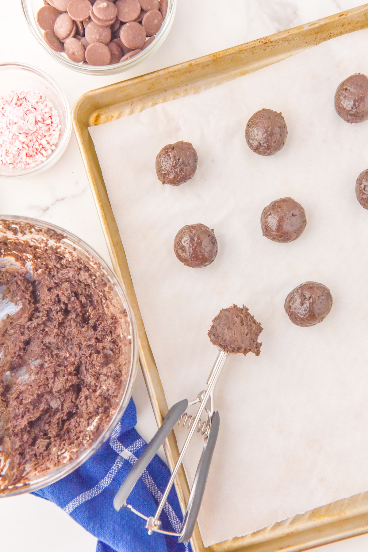 Chocolate balls being placed on a cookie sheet with a cookie scoop