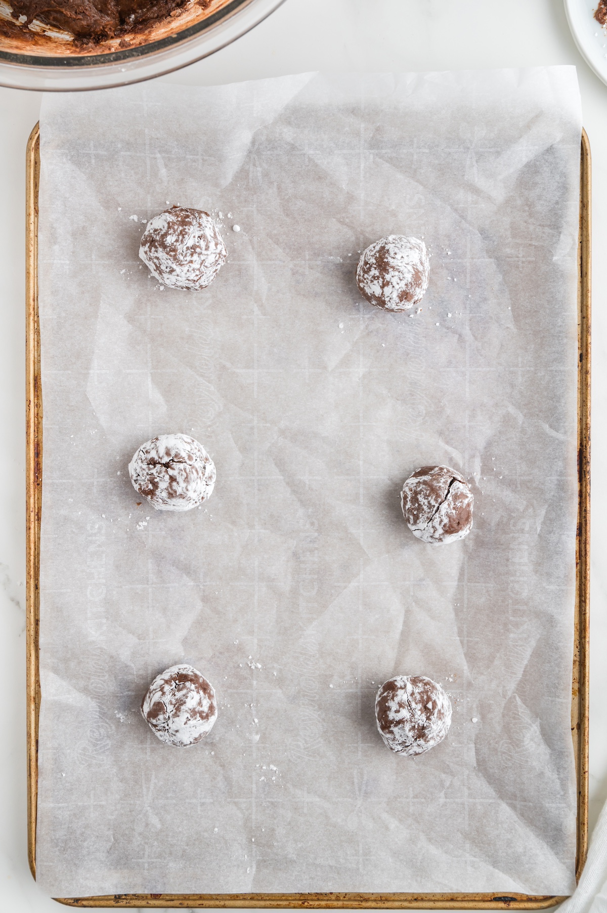 rolled chocolate dough balls placed on a baking sheet covered in parchment paper