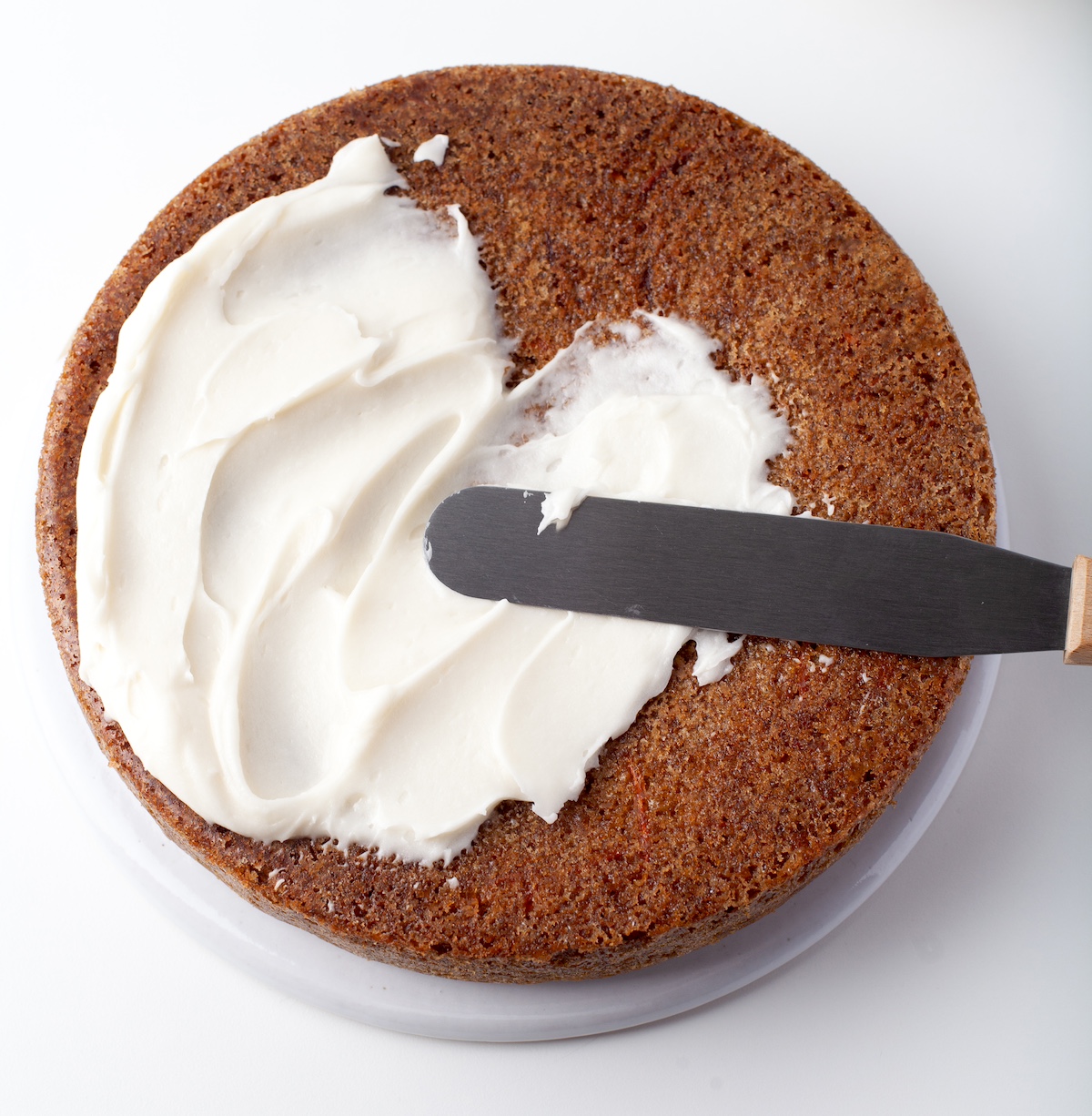Frosting a carrot cake with cream cheese frosting