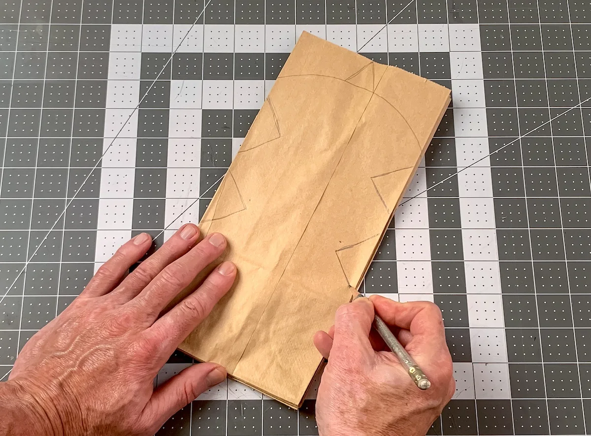 Hand drawing a design with a pencil on a stack of glued paper bags