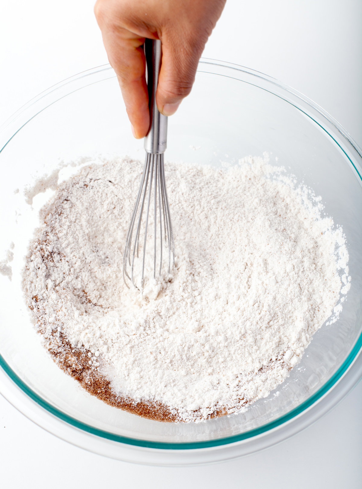 Hand using a whisk to mix flour, sugars, baking soda, cinnamon, and salt.