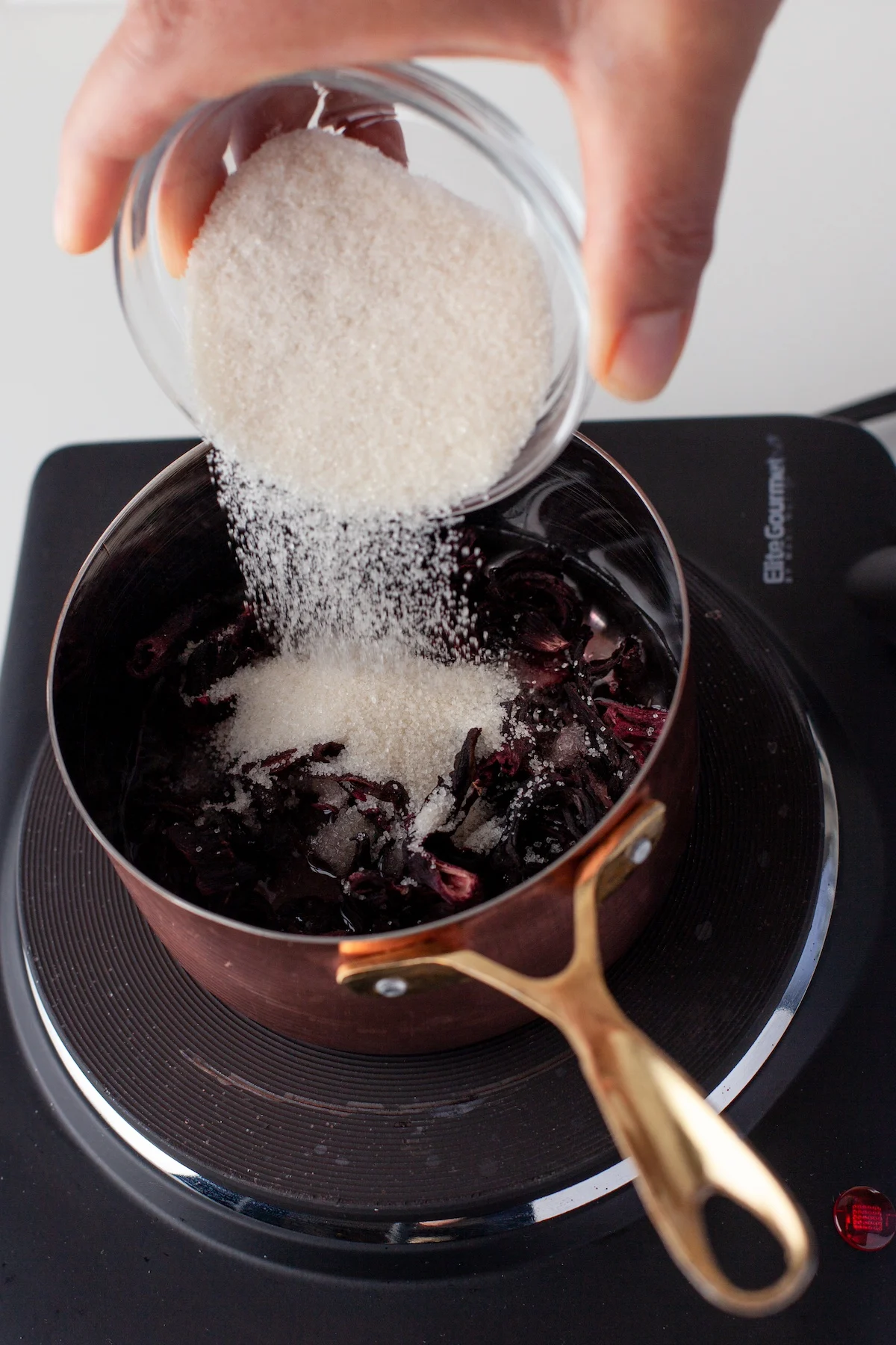 Pouring sugar into a saucepan with water and hibiscus flowers