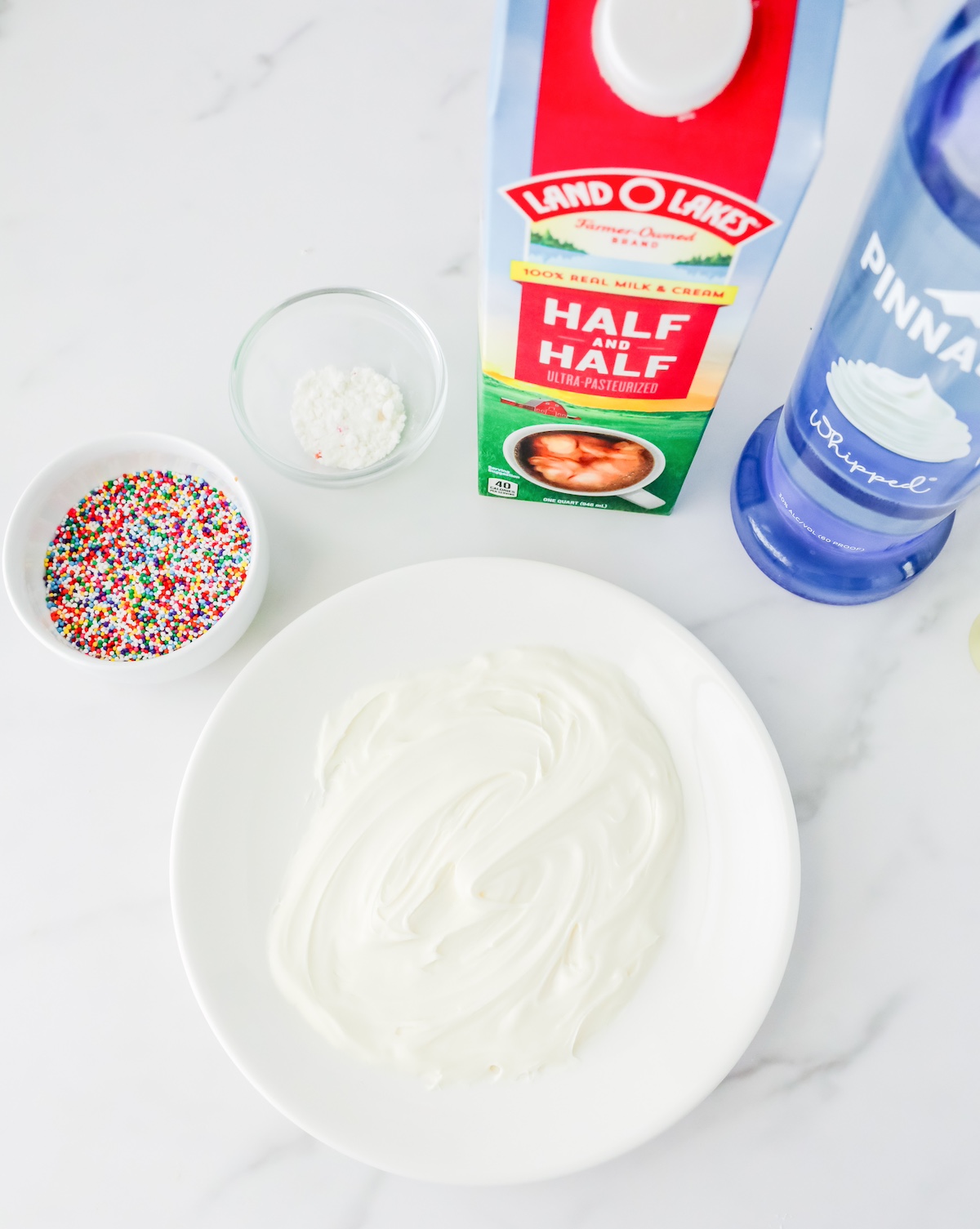 Sprinkles, half and half, whipped cream vodka, and vanilla icing on a white plate