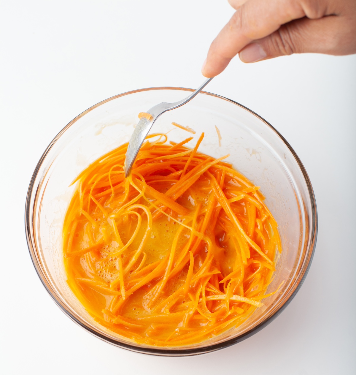 stirring carrots into a mixture of eggs, oil, and vanilla