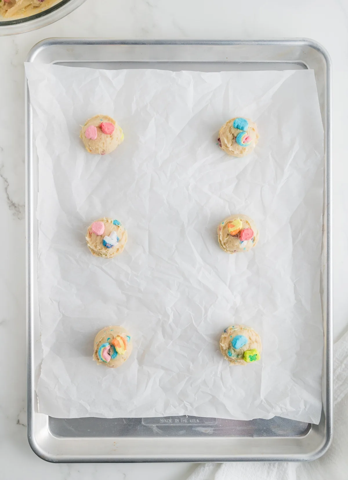 Scooped lucky charm dough on a parchment paper covered cookie sheet