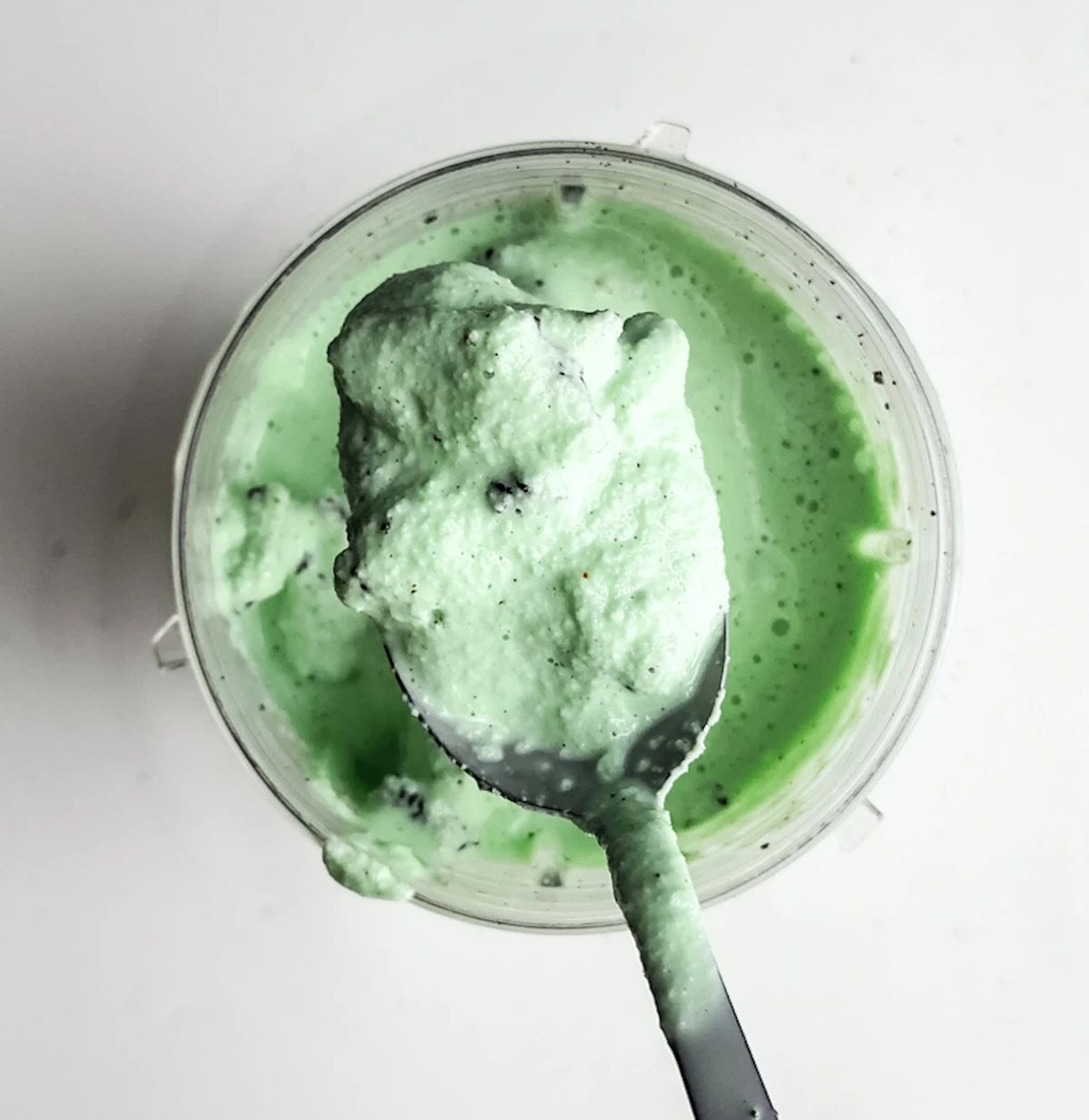 Spoon holding green milkshake with Oreo above the glass