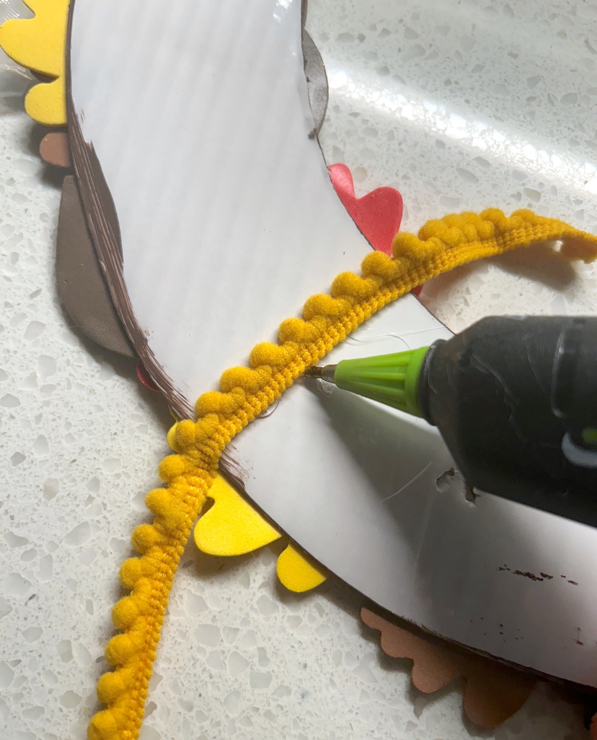 gluing pom pom trim to the back of the cardboard